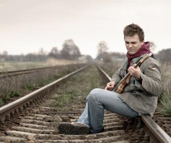 man sat on railway track playing guitar